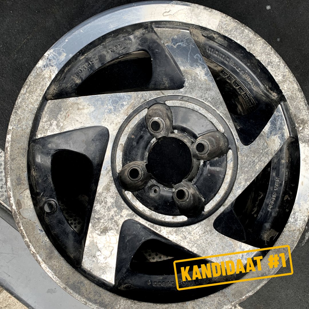Een zwaar beschadigde zwarte velg vol vuil en corrosie, met het stempel Kandidaat 1